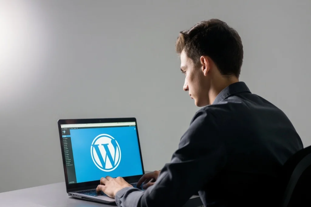 Developer working on laptop displaying WordPress icon in professional studio setting